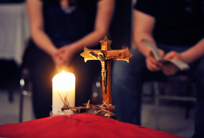 Two people standing beside a lighted candle and a crown of thorns.